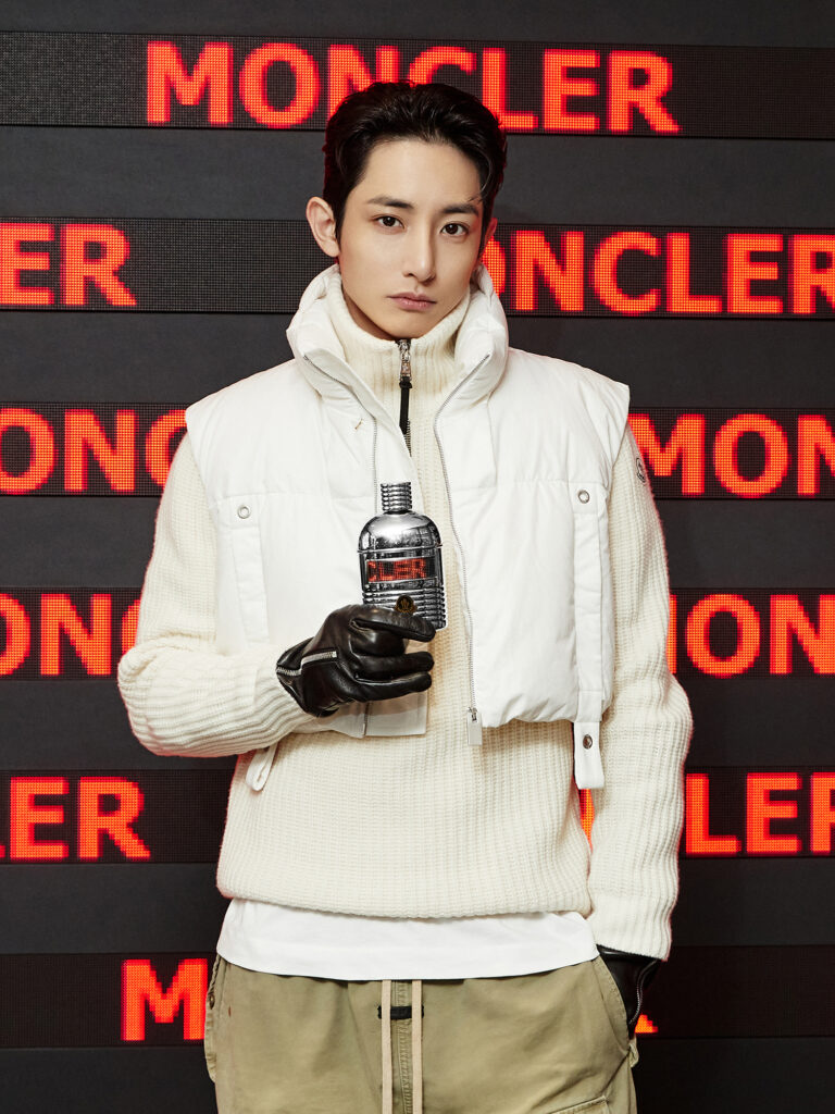 몽클레르 애드버토리얼 촬영. 레드 LED MONCLER 타이포 배경 앞에서 셀러브리티가 Pour Homme 향수 보틀을 들고 있는 상반신 클로즈업.